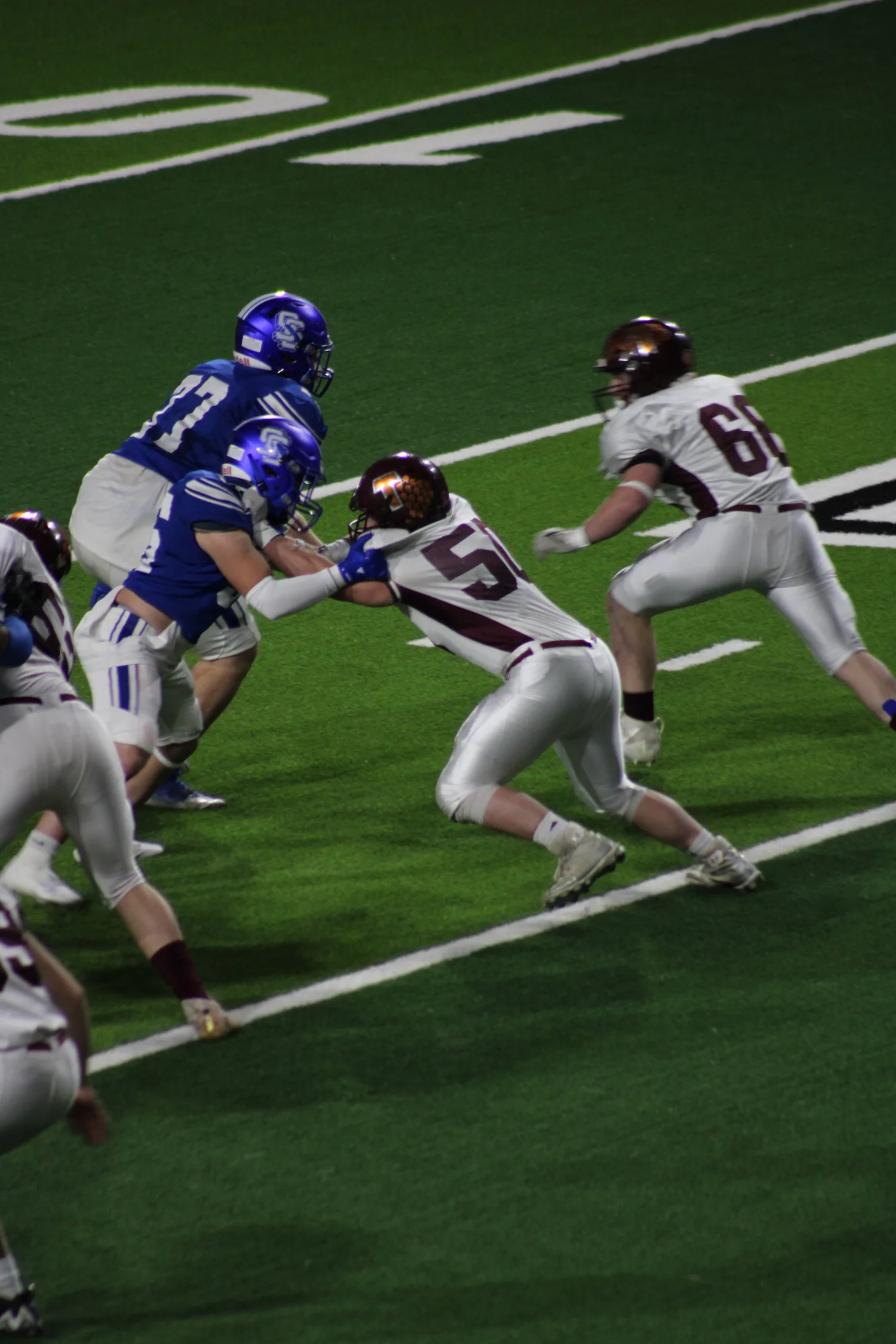 High school football players rushing toward the end zone under the lights