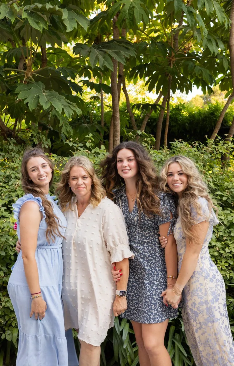 Mother and three daughters smiling together in front of green foliage