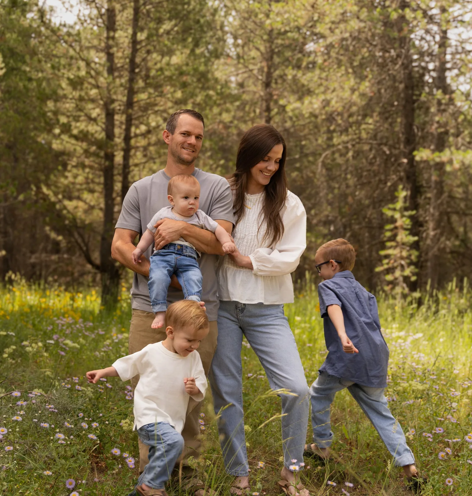 Playful family photo of parents and three young boys in a sunlit forest