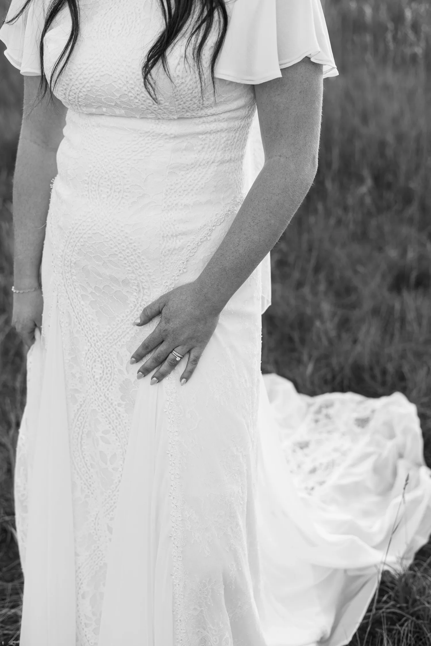 Black-and-white detail of a bride's hand resting on her lace dress