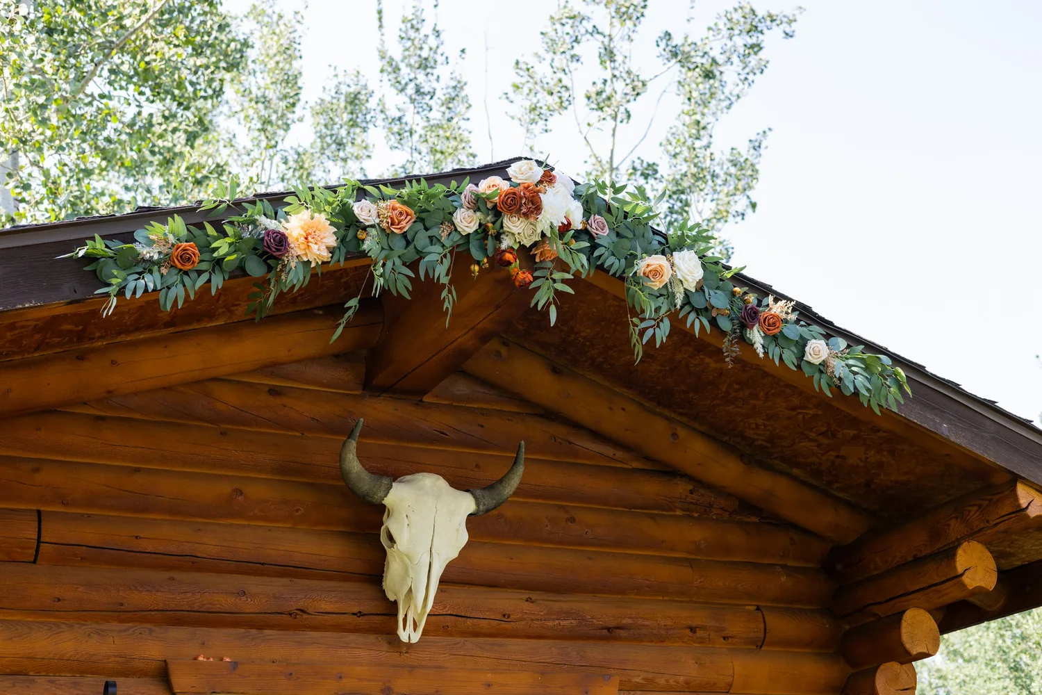 Log cabin roof decorated with a flower garland and a steer skull for a rustic wedding