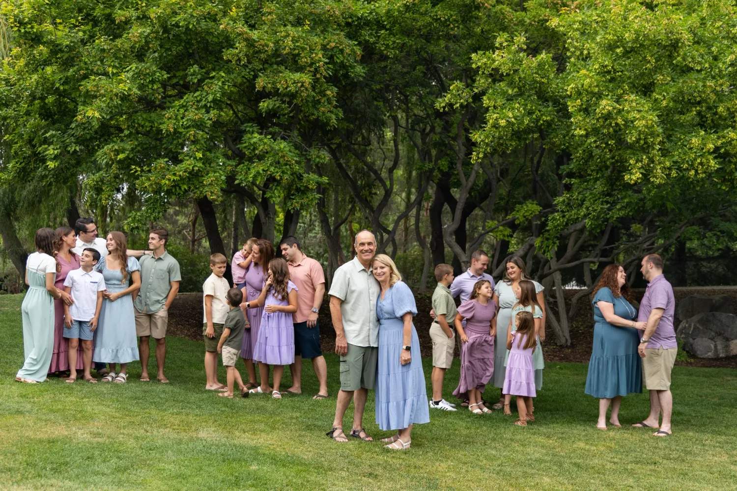 Large family group portrait on a lawn under green trees