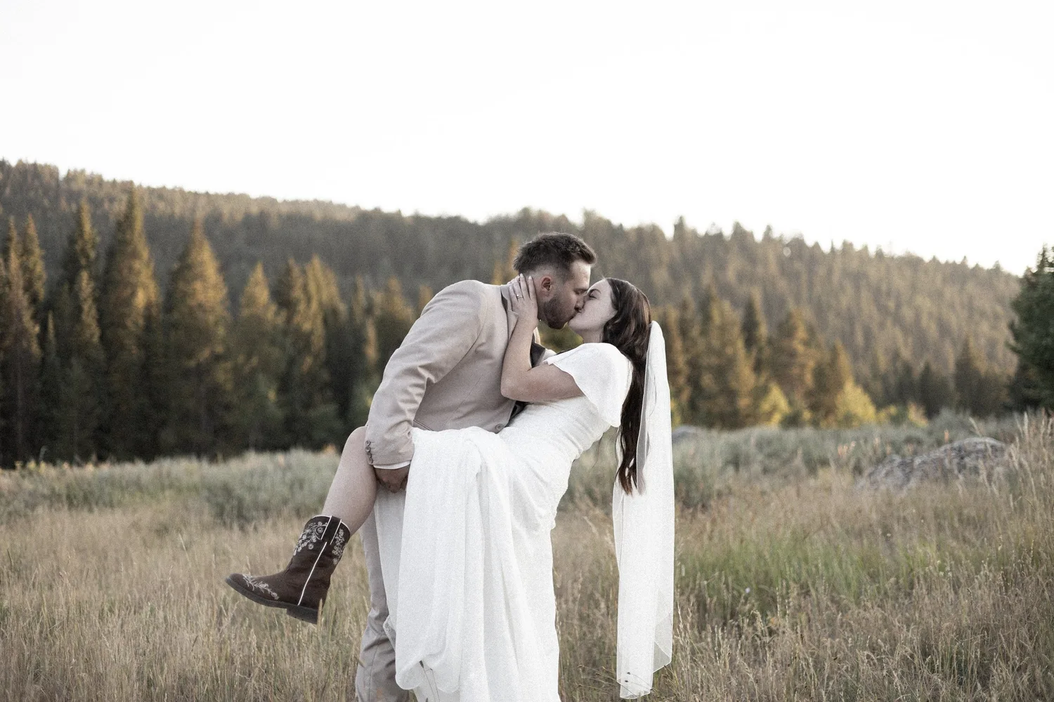 Groom lifting and kissing his bride in a mountain meadow at golden hour