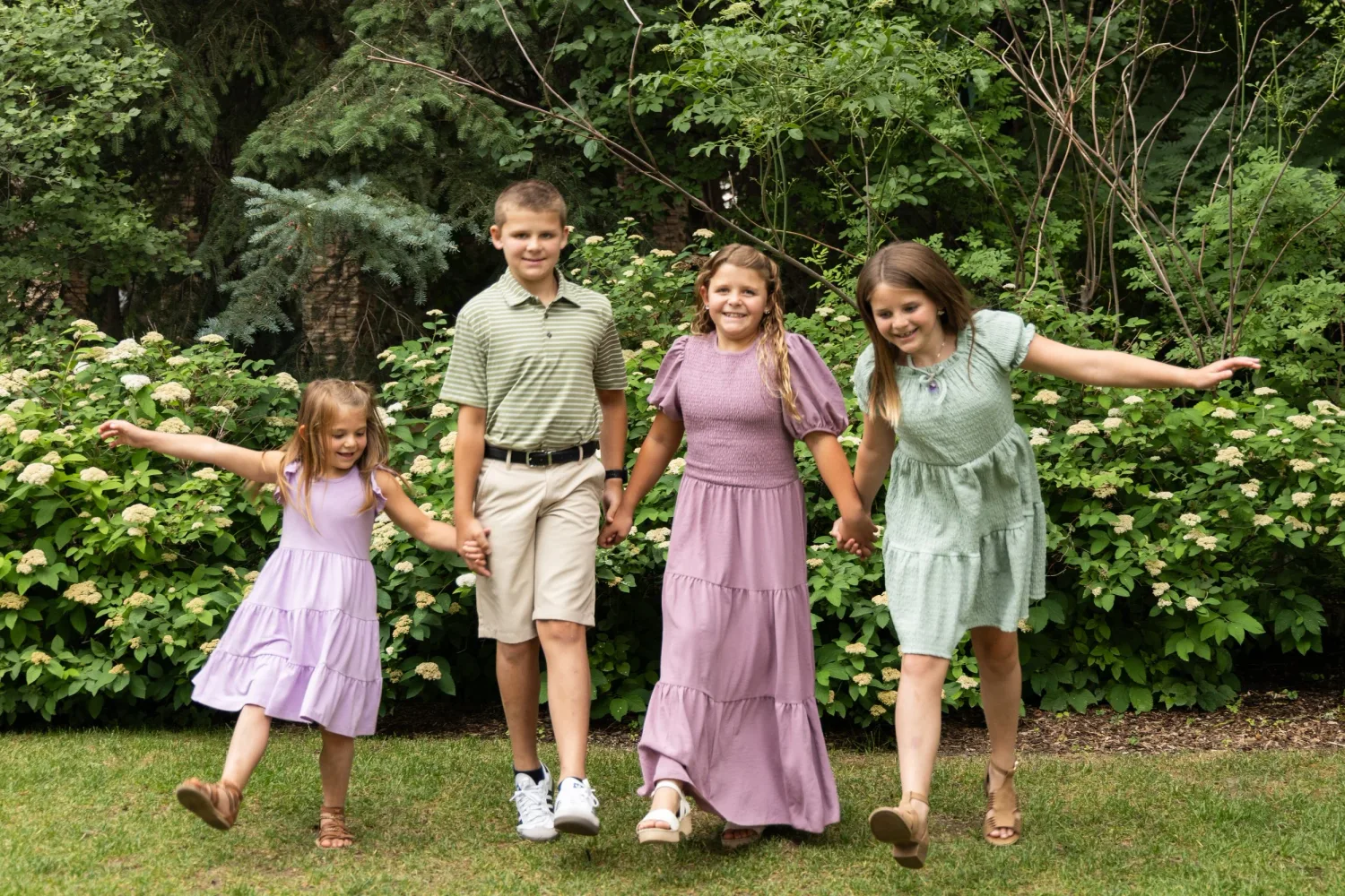 Four siblings dancing and leaping on a lawn