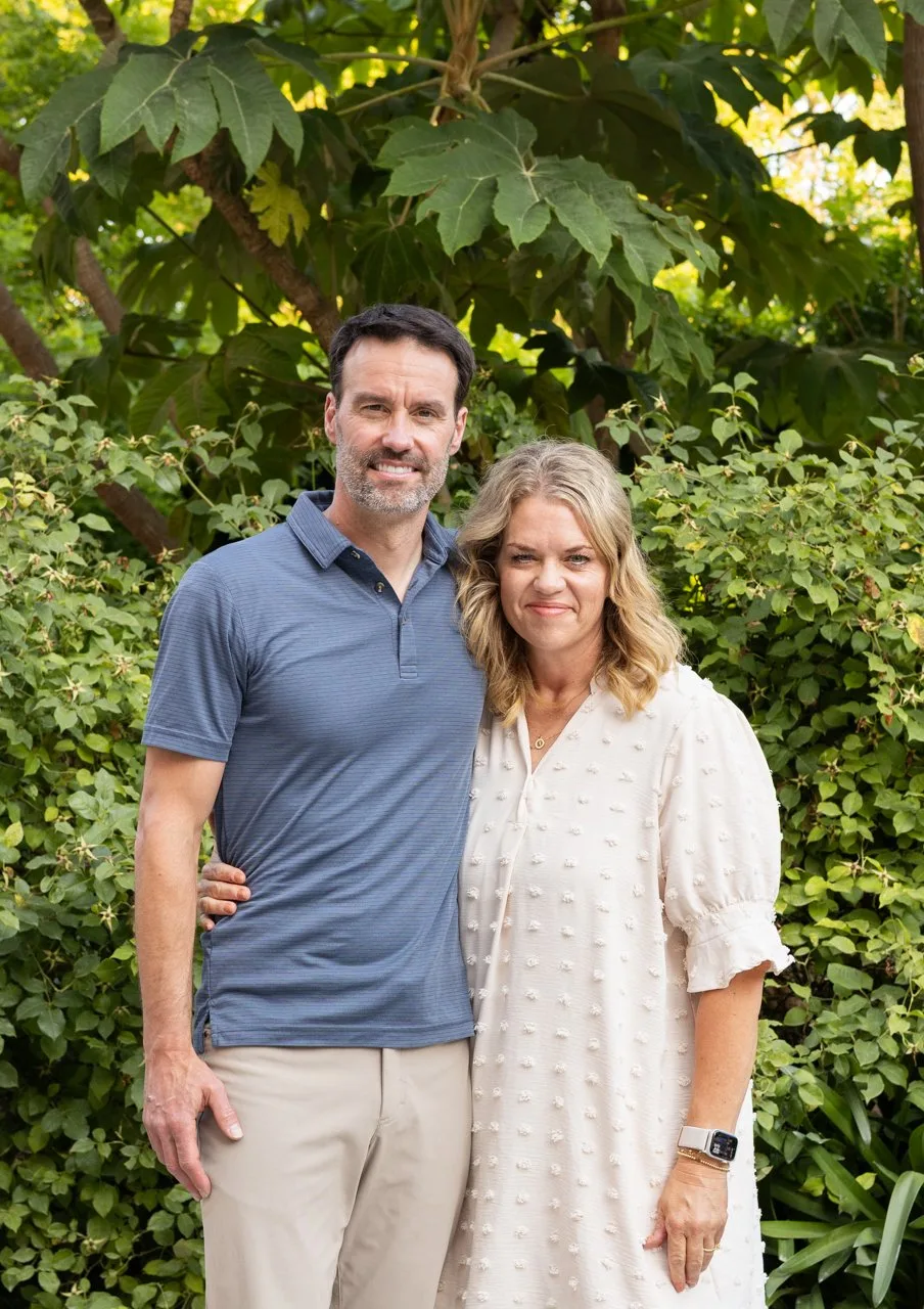 Couple smiling together in front of large green leaves