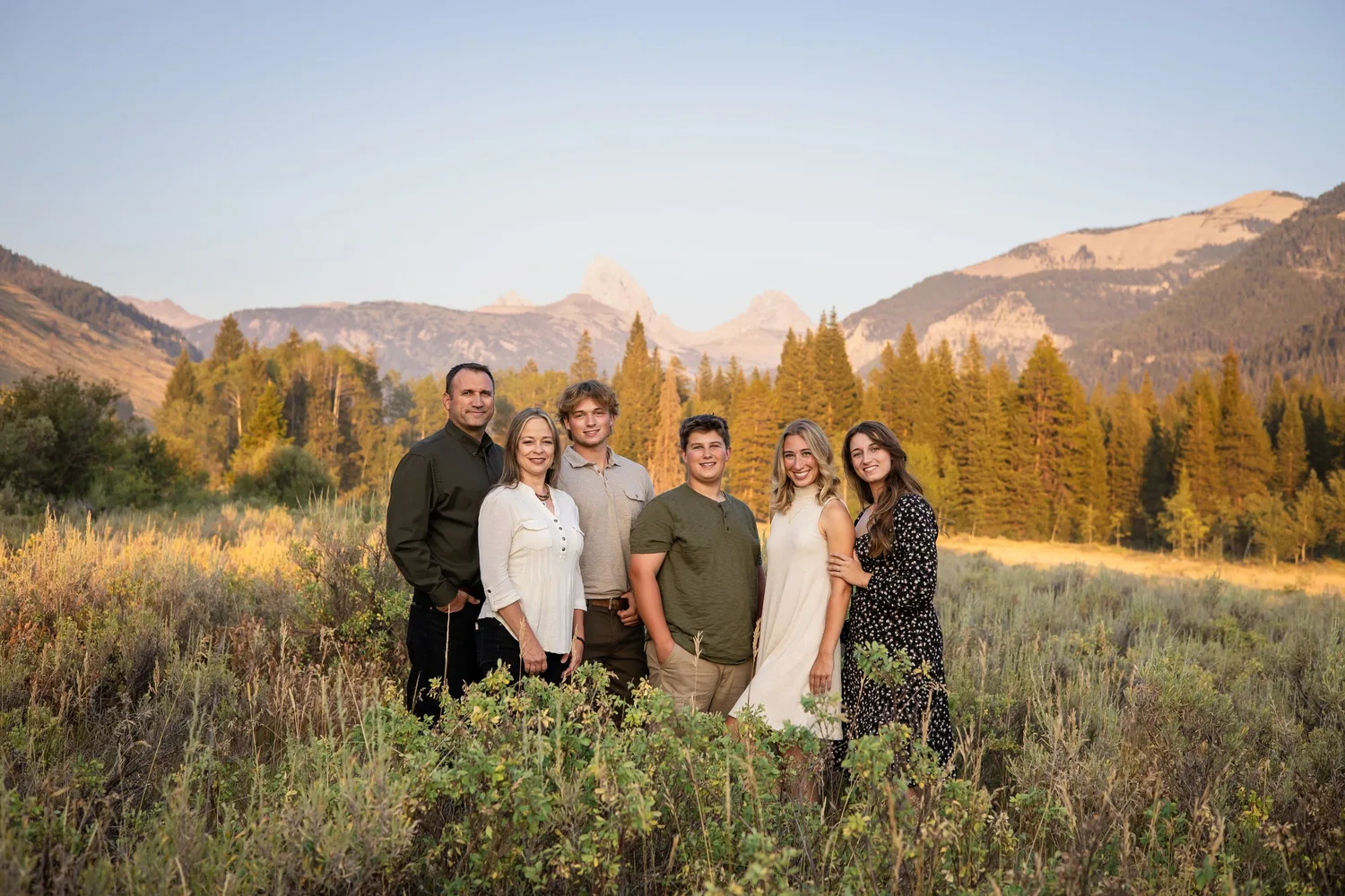Family of six in a meadow at sunset with mountains behind them