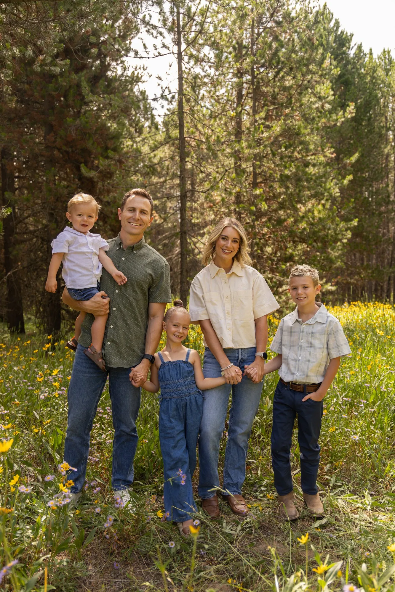 Family of five with a toddler in a wildflower field among pine trees