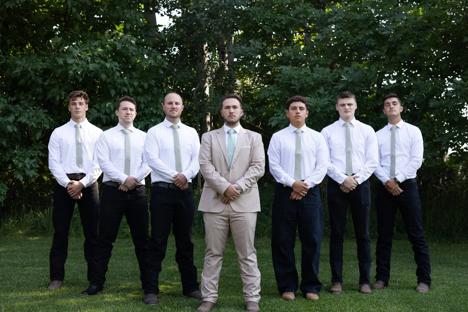 Groom in a tan suit standing with his groomsmen in white shirts and sage ties