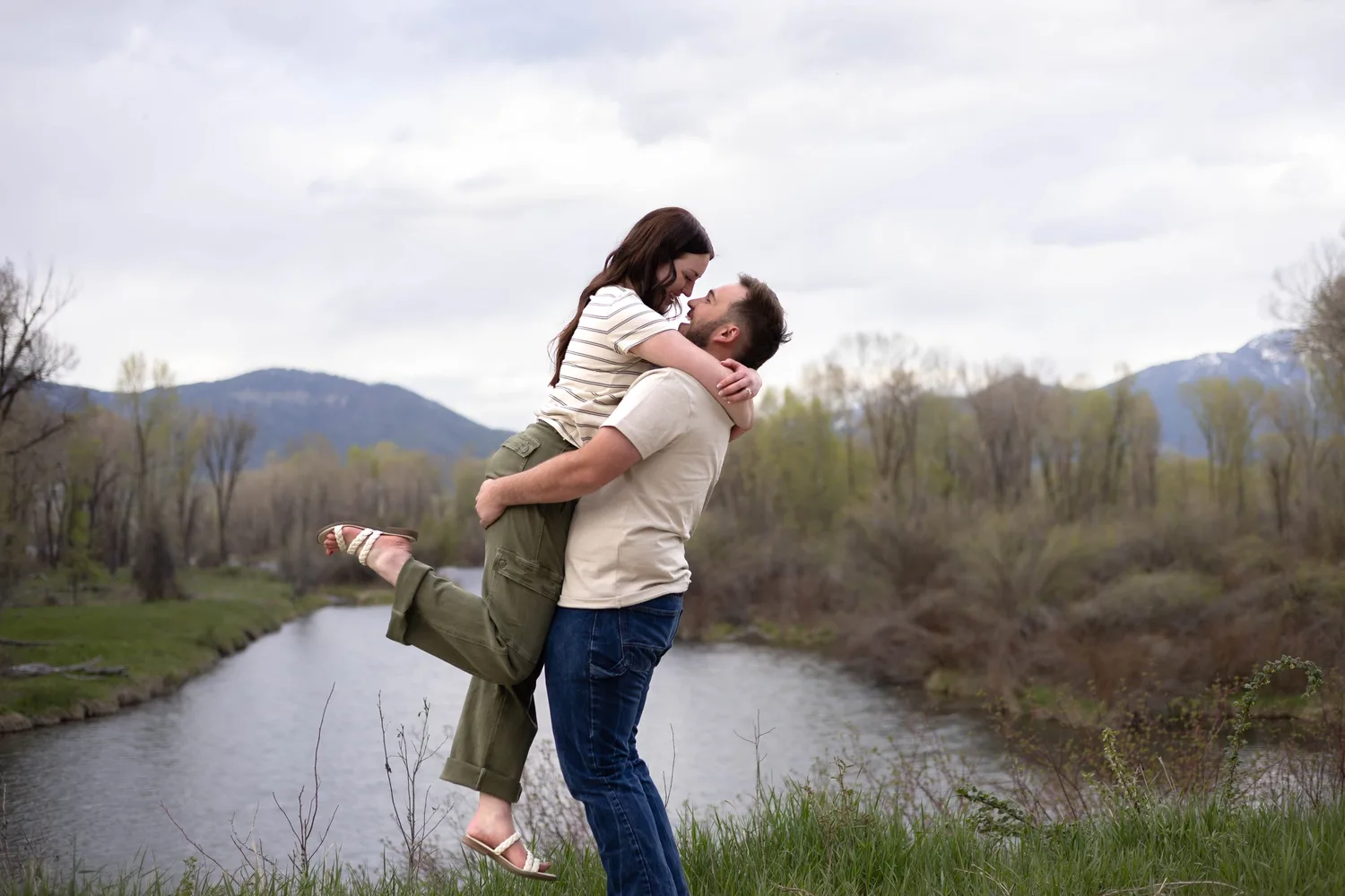 Woman jumping into her fiancé's arms beside a river in spring