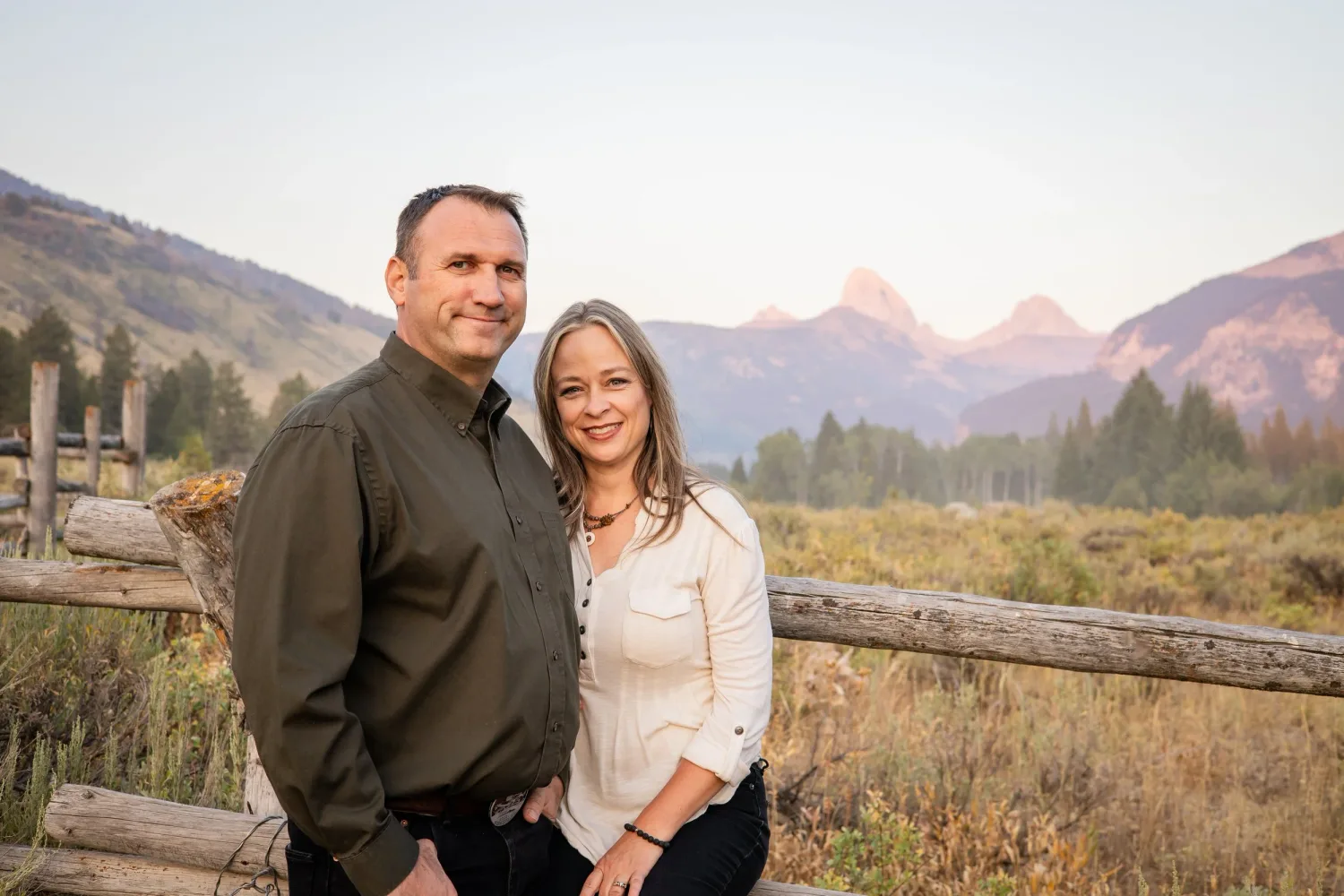 Couple by a wooden fence with the Grand Tetons in the background