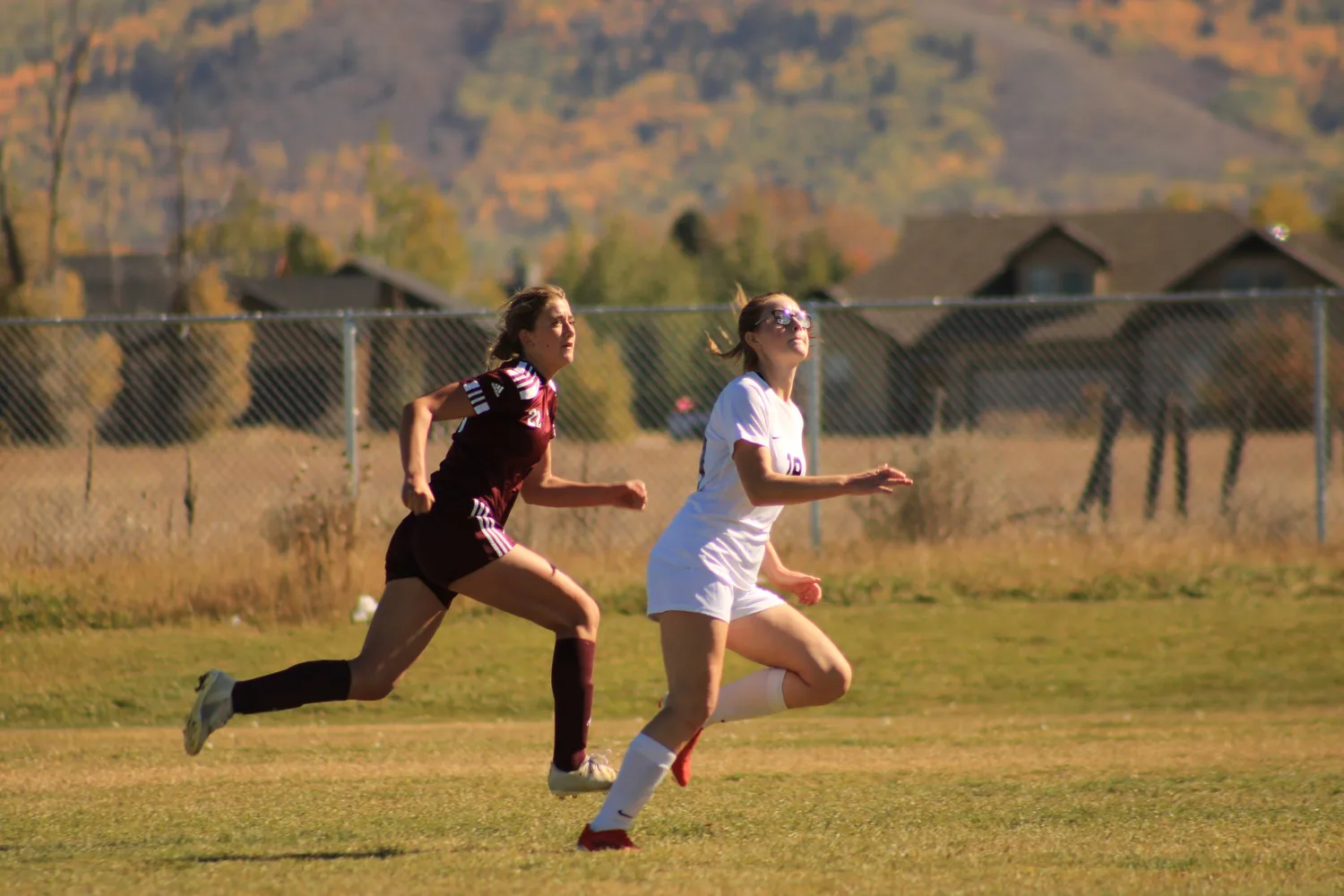 Two girls' soccer players racing for the ball with autumn hills behind them