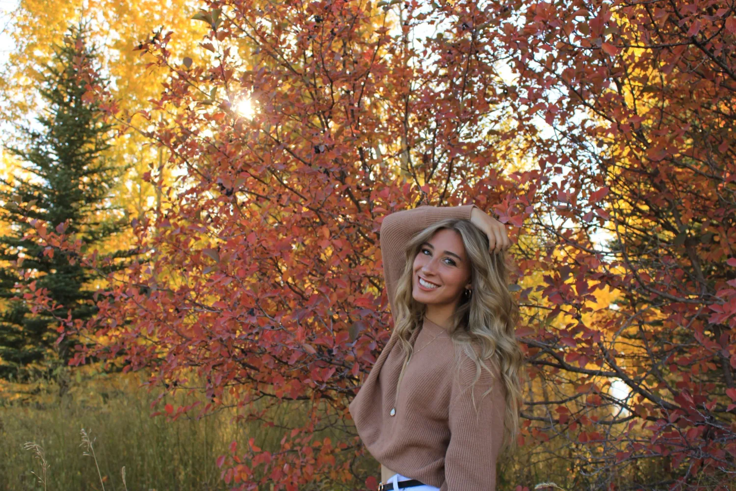 Senior portrait of a young woman in a tan sweater among red and orange autumn trees