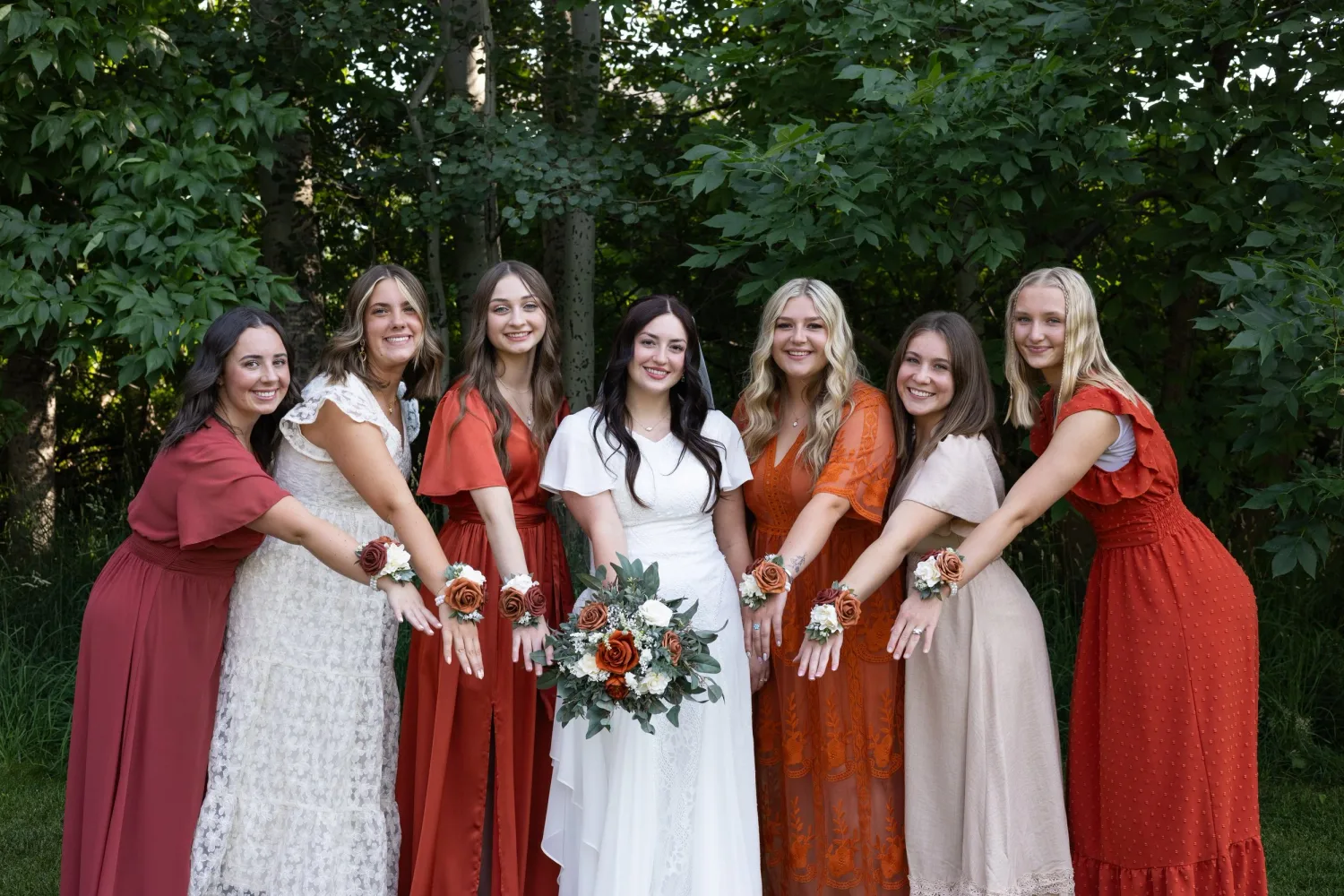 Bride with her bridesmaids in rust and blush dresses showing their wrist corsages