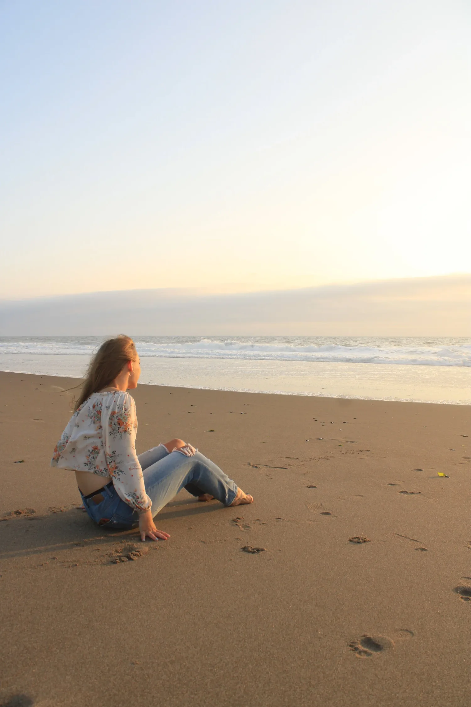 Young woman sitting on the beach looking out at the ocean at sunset