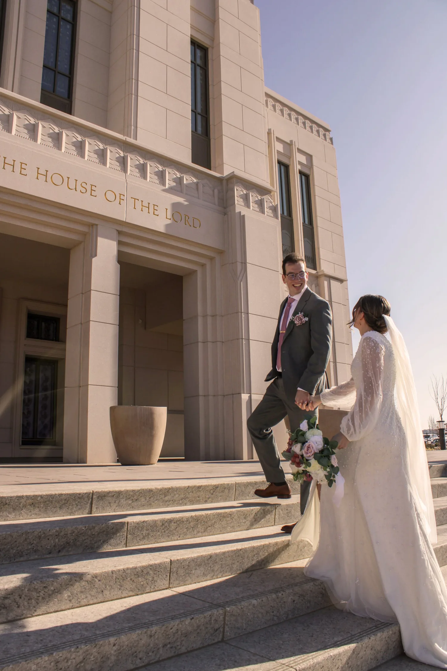 Bride and groom walking up the steps of a temple, her long veil trailing behind