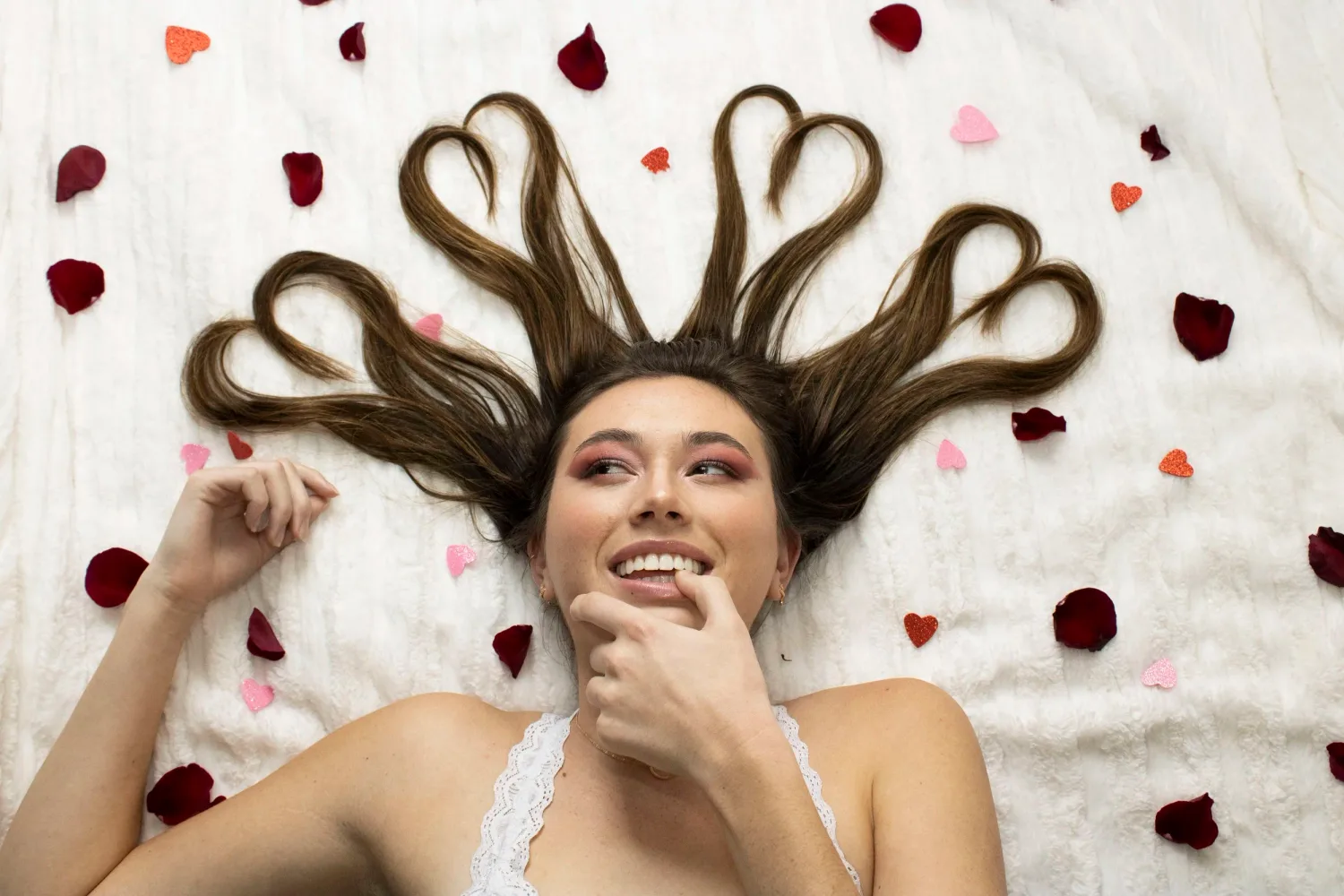 Creative portrait of a smiling young woman with her hair shaped into hearts among rose petals