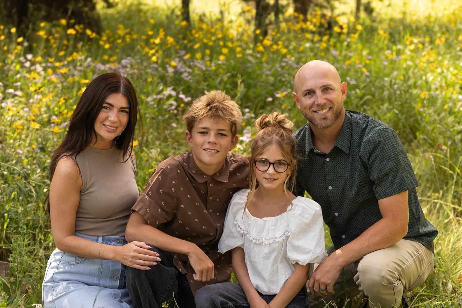 Family of four kneeling together in a field of yellow wildflowers