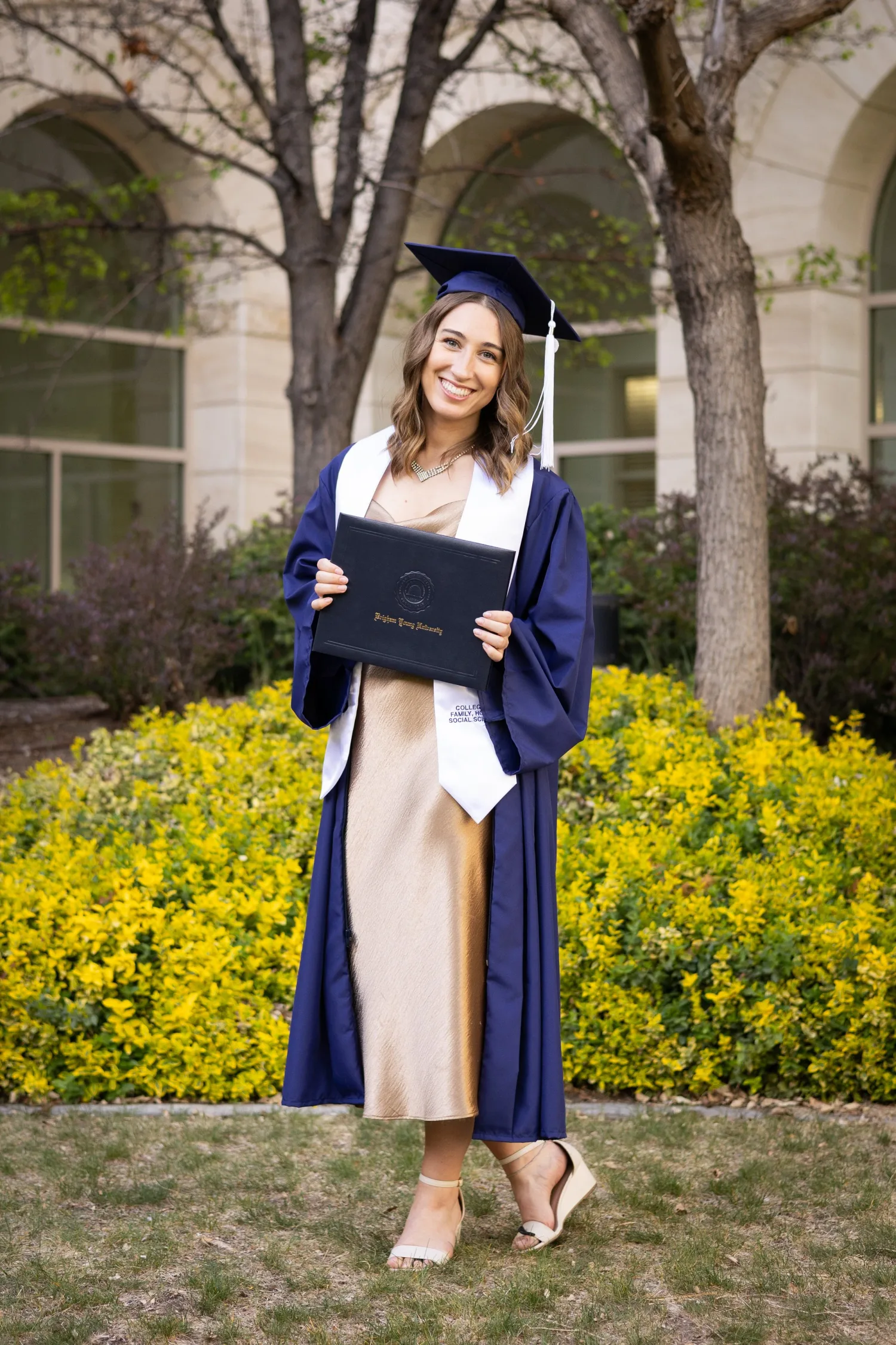 College graduate in a navy cap and gown smiling with her diploma