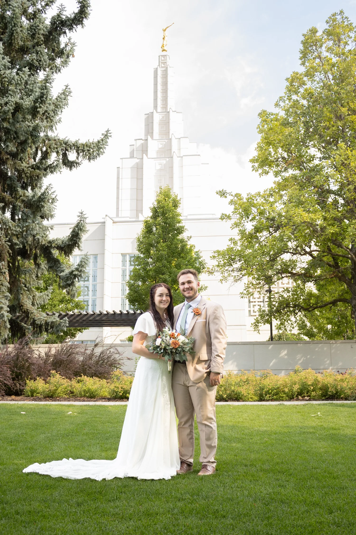 Bride and groom on the lawn in front of a white temple with a tall spire