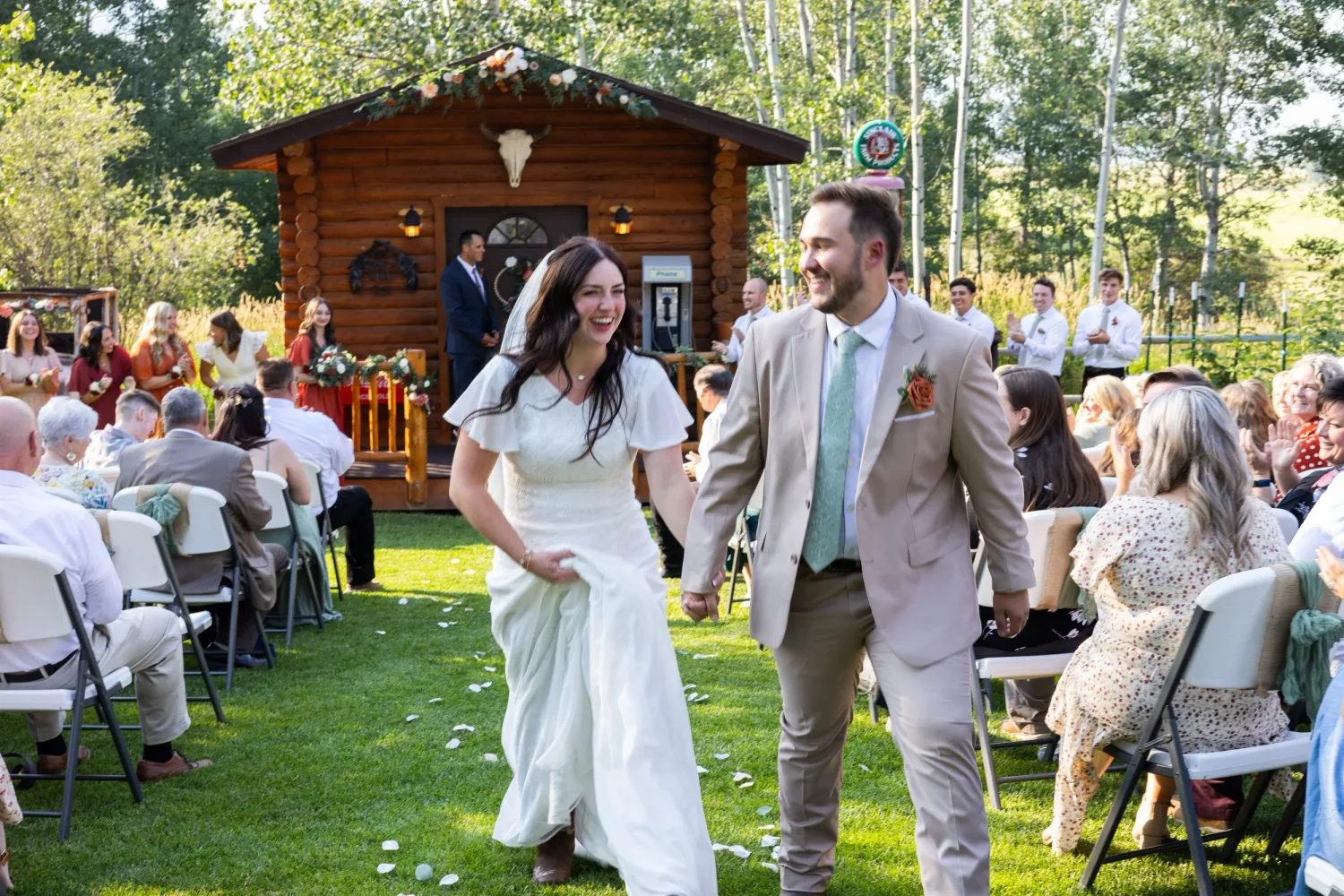 Bride and groom walking back up the aisle, laughing, at an outdoor cabin wedding