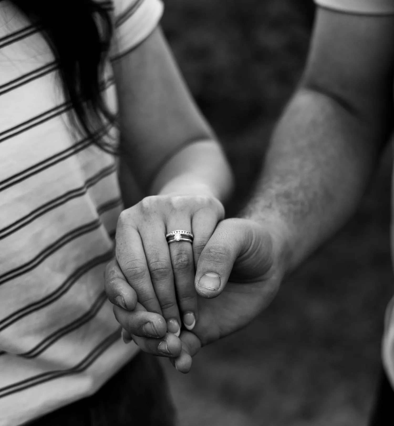Black-and-white close-up of a couple holding hands, showing her engagement ring