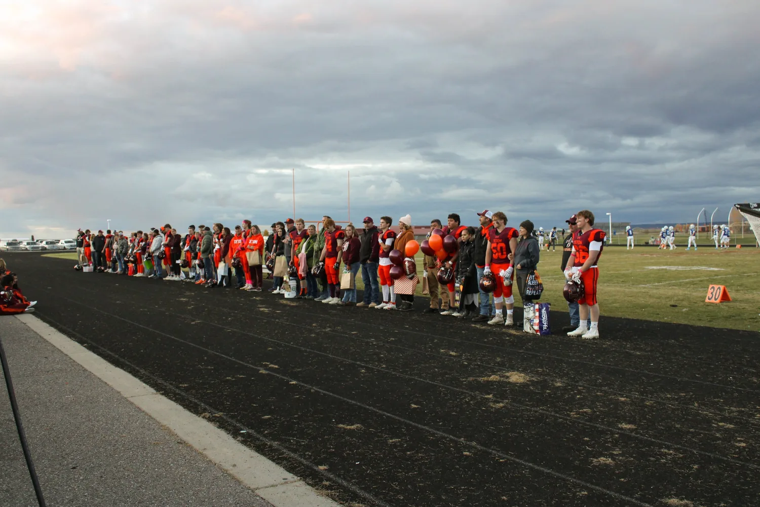 Football team lined up along the sideline under a cloudy sky