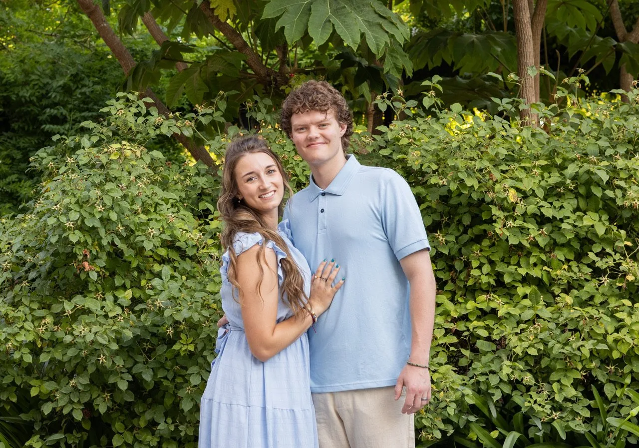 Couple in light blue outfits posing in front of green shrubs