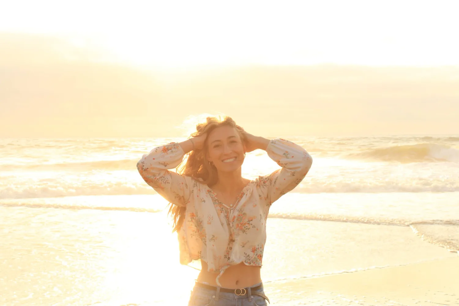 Young woman on a bright sunlit beach with her hands in her hair