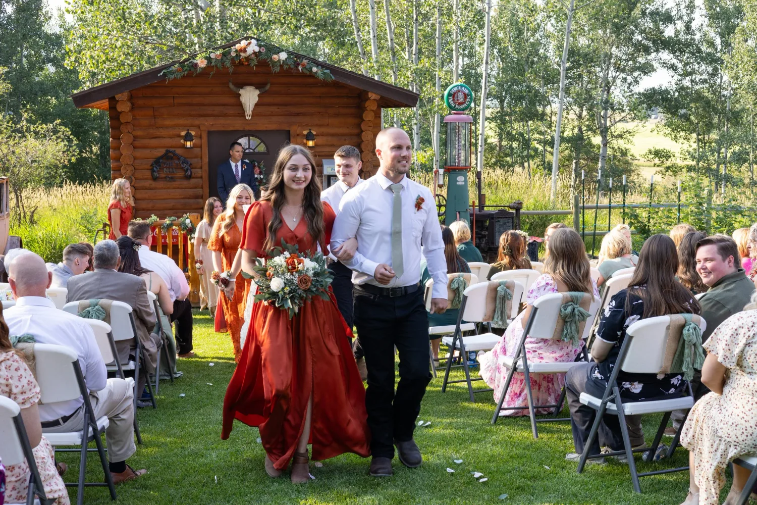 Bridesmaid and groomsman walking down the aisle at an outdoor cabin wedding