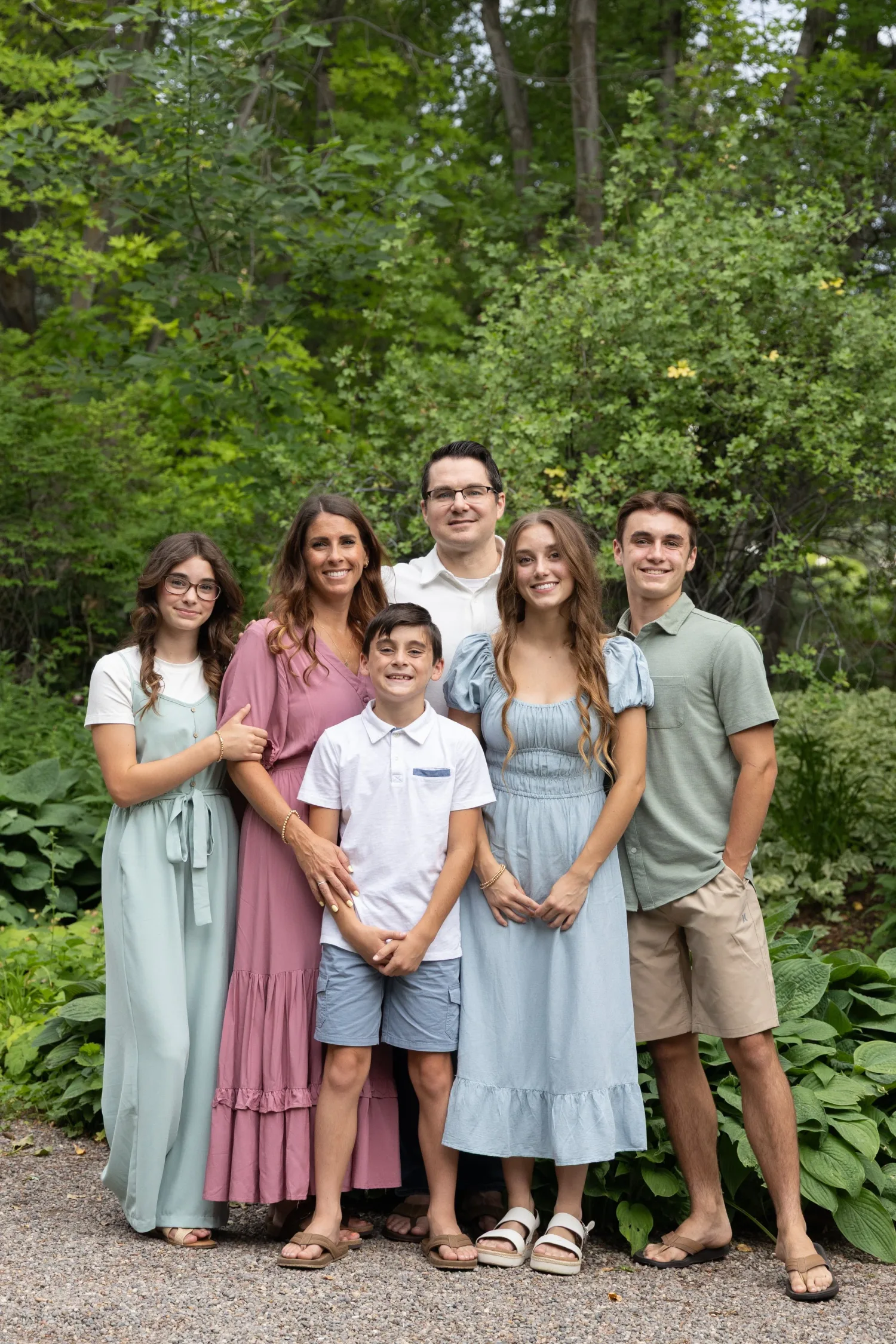 Family of seven in pastel outfits posing among green trees