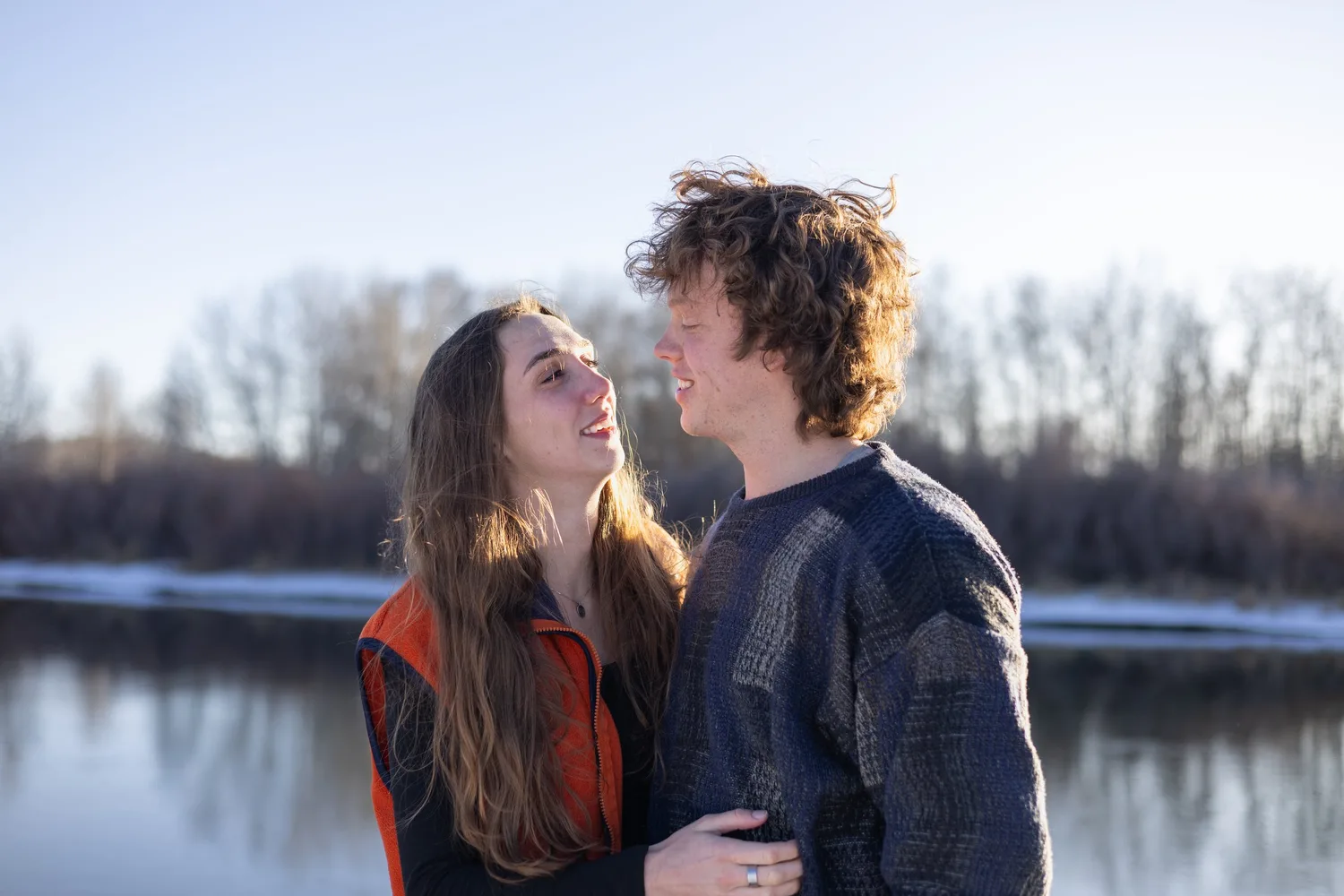 Couple smiling at each other by a river on a winter afternoon