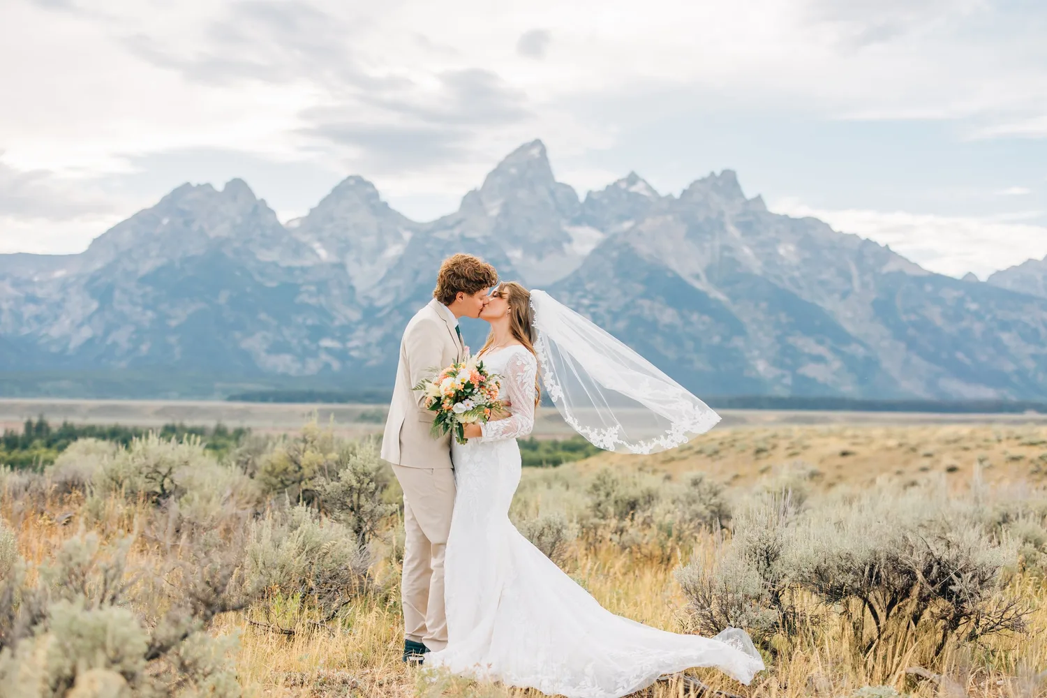 Bride and groom kissing in a sagebrush field with the Grand Teton mountains behind them