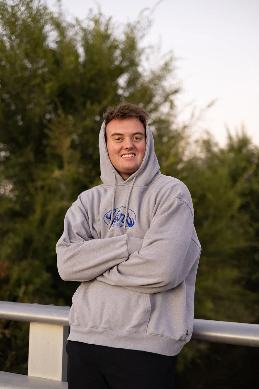 Senior portrait of a smiling young man in a gray hoodie leaning on a bridge railing