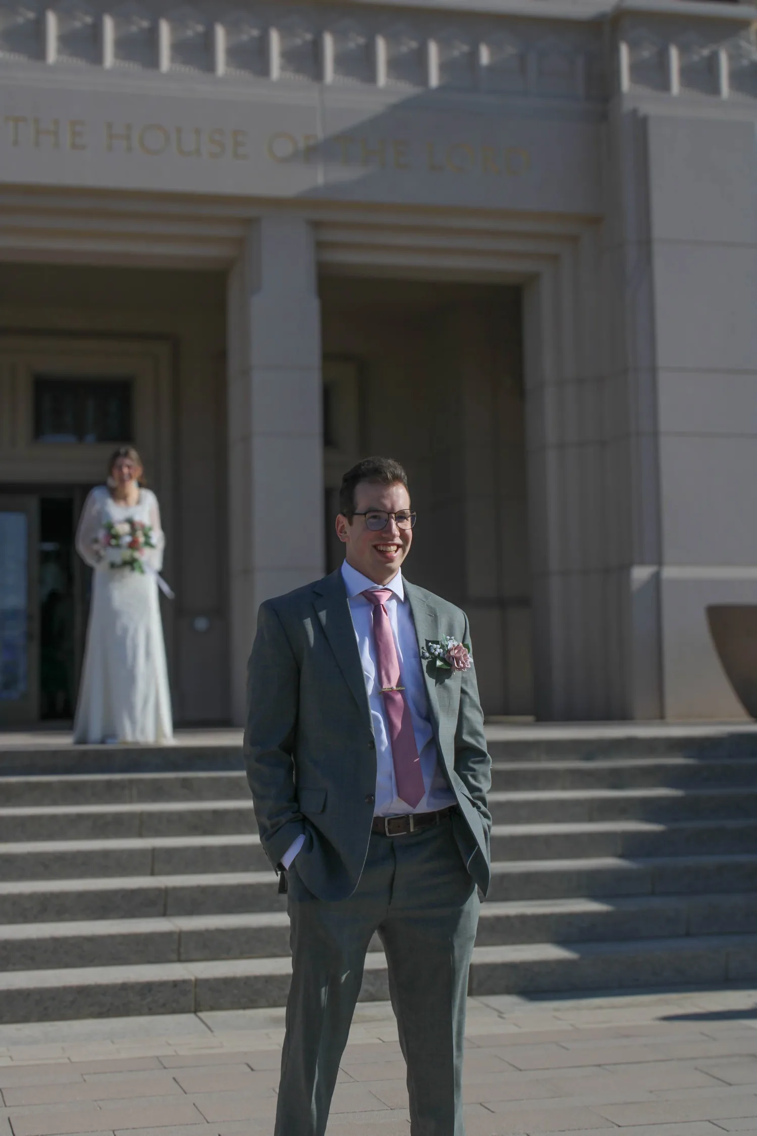 Groom smiling while his bride waits on the temple steps behind him