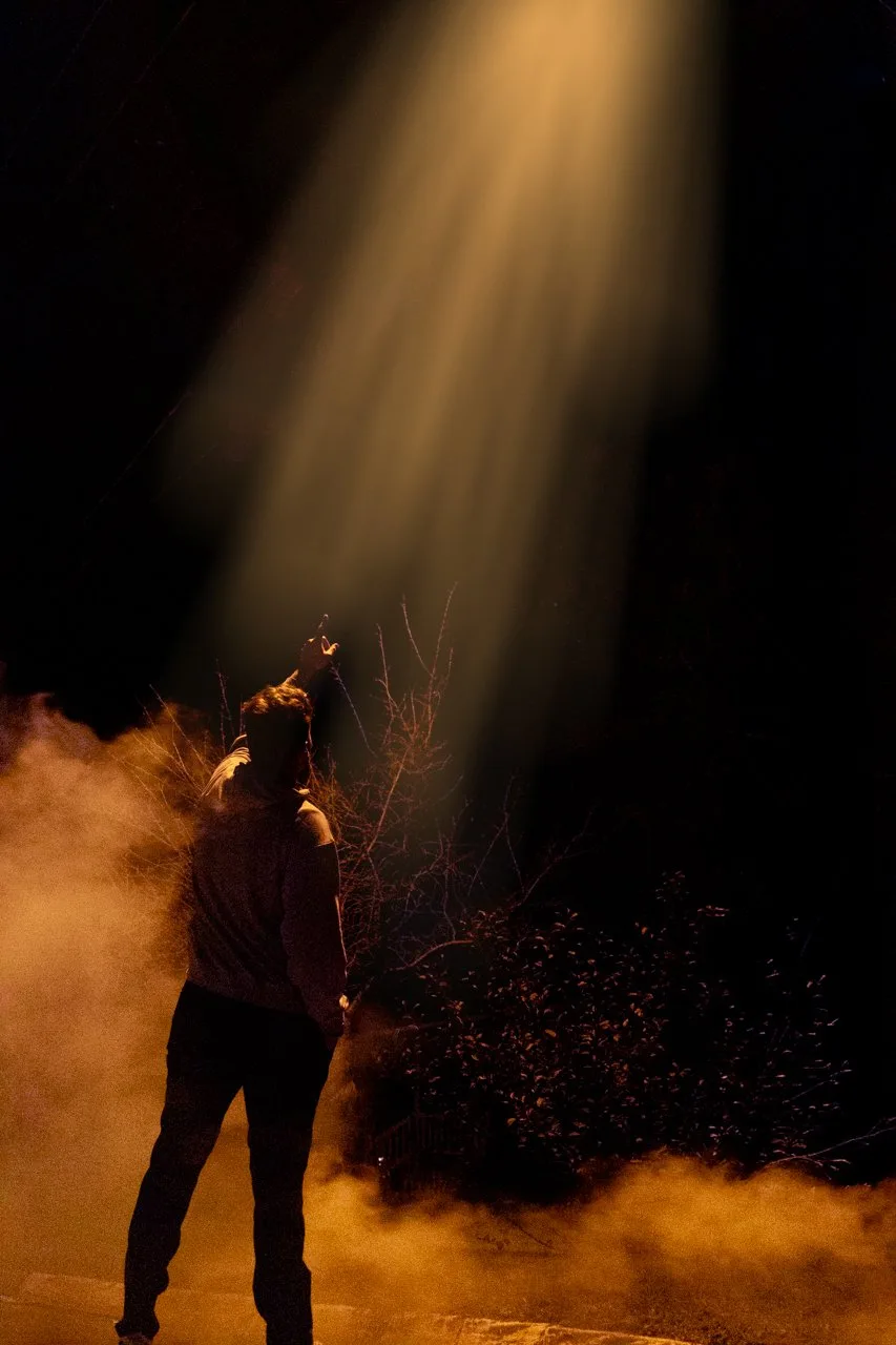 Person standing in a beam of light and orange smoke at night