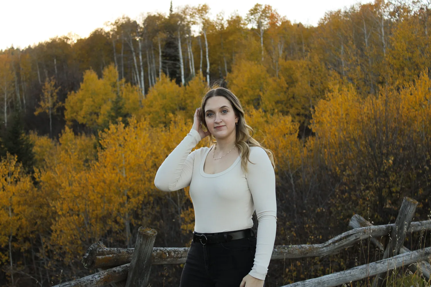 Portrait of a young woman by a split-rail fence with golden aspen trees behind her
