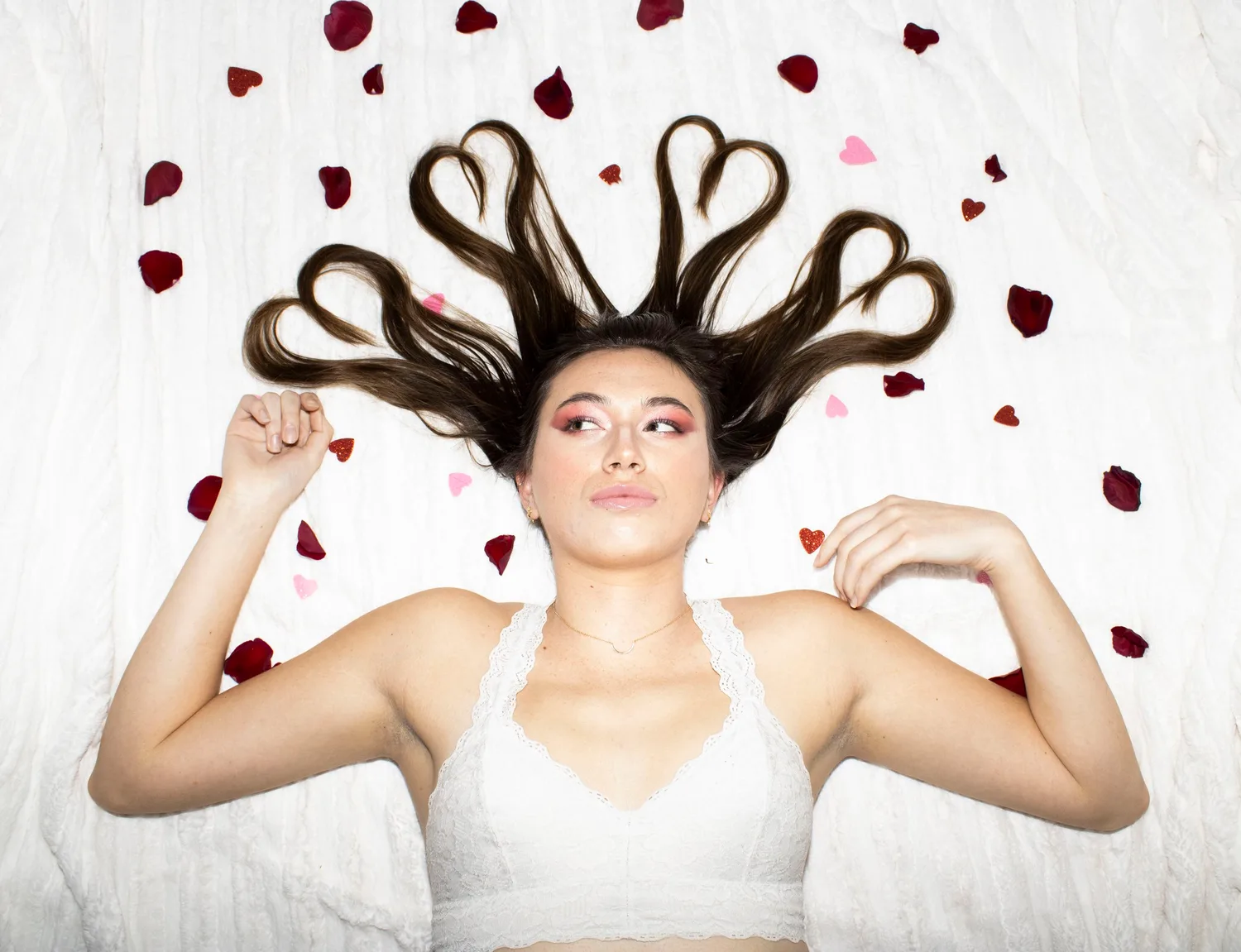 Creative portrait of a young woman lying down with her hair shaped into hearts among rose petals