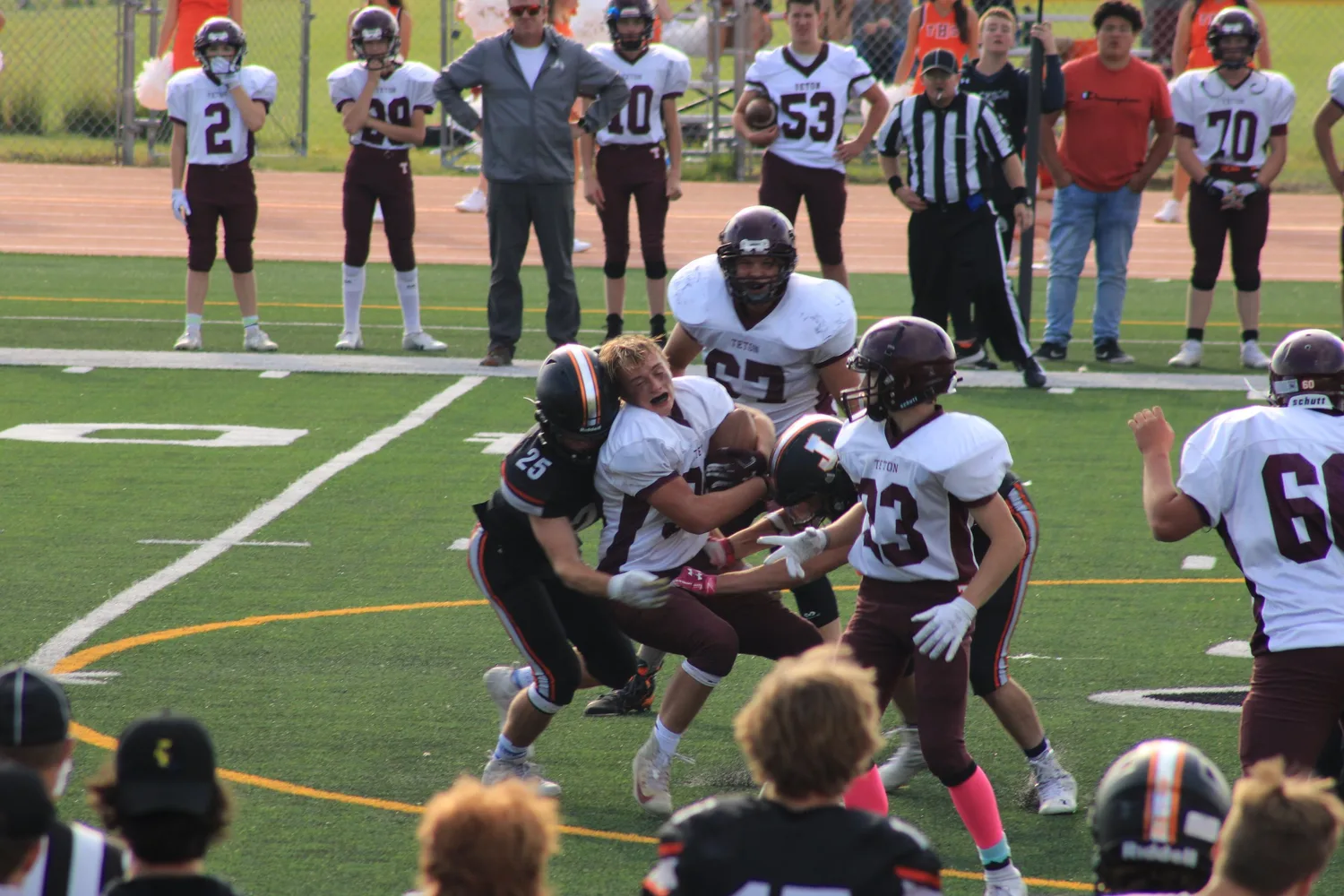 High school football players blocking as teammates watch from the sideline