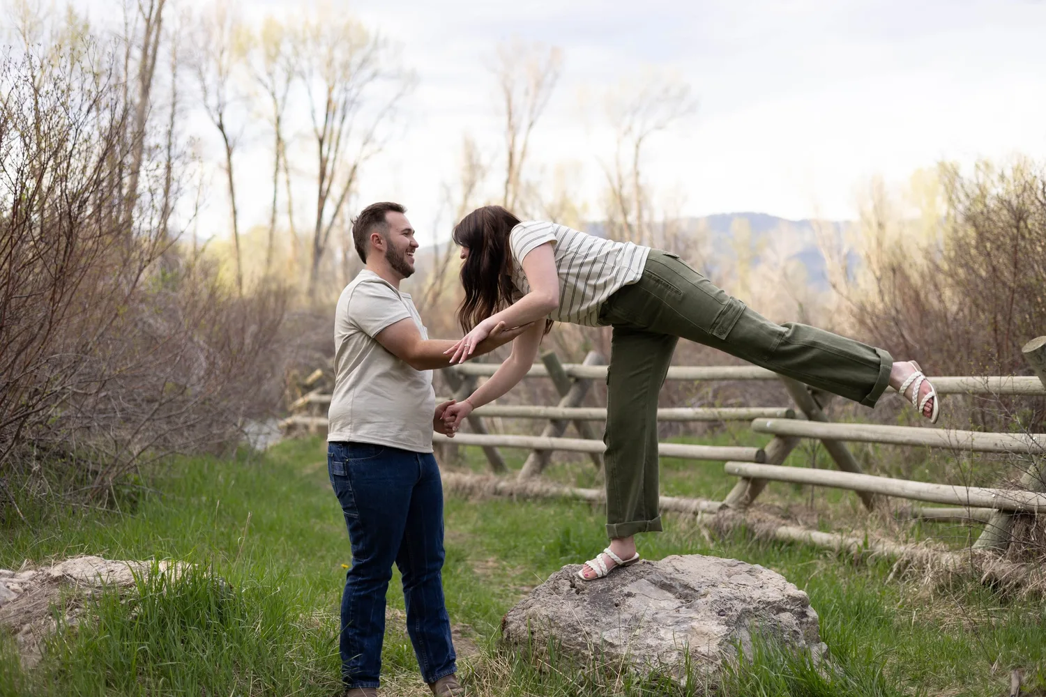 Playful couple dancing by a split-rail fence in the spring