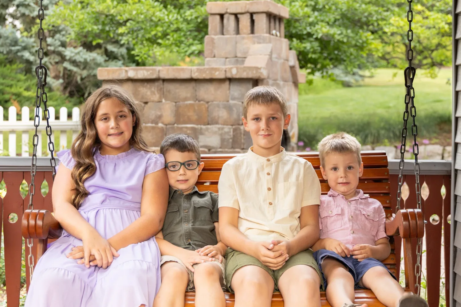 Four young siblings sitting together on a porch swing