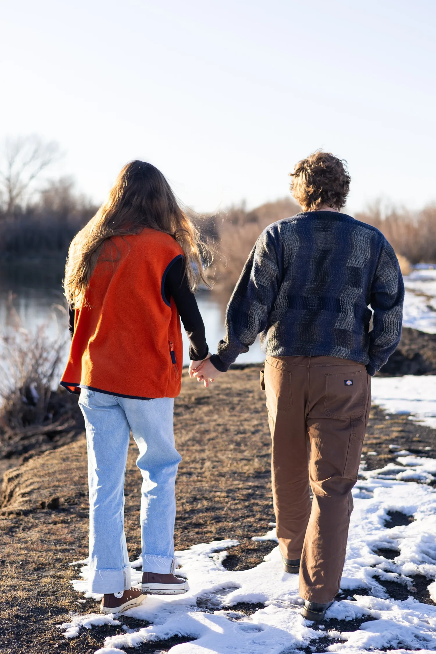 Couple walking hand in hand along a snowy riverbank