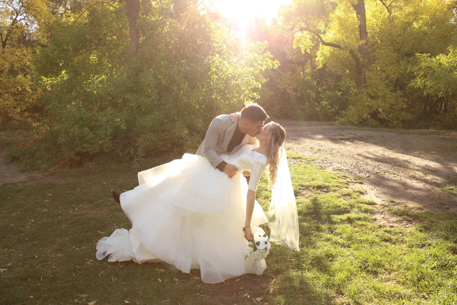 Groom dipping and kissing his bride on a sunlit autumn path