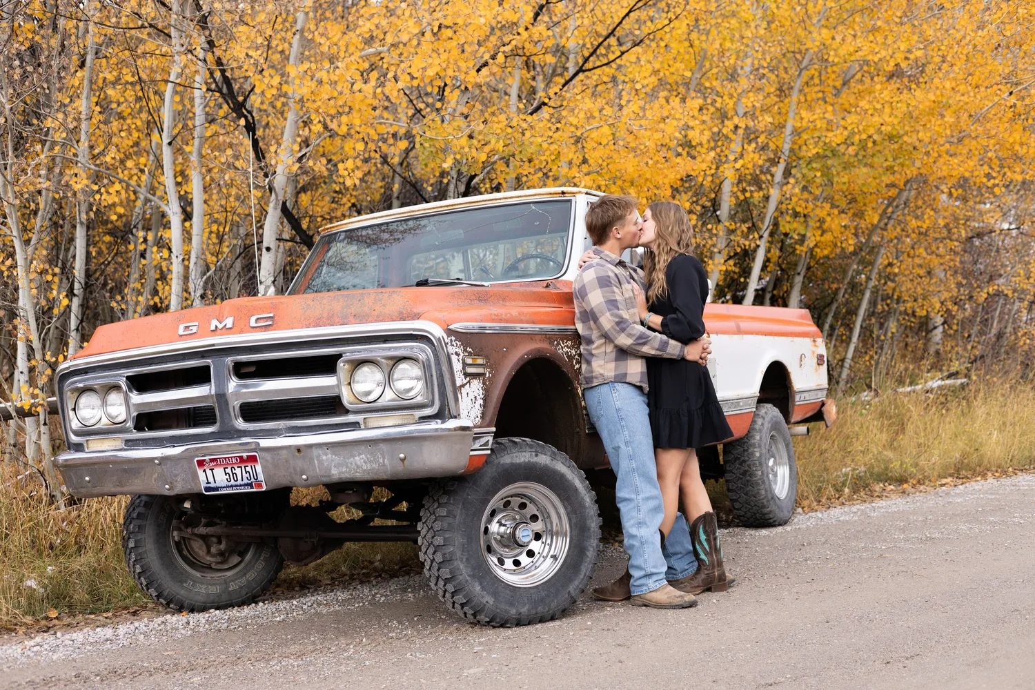 Couple kissing against a vintage orange GMC pickup among golden aspens