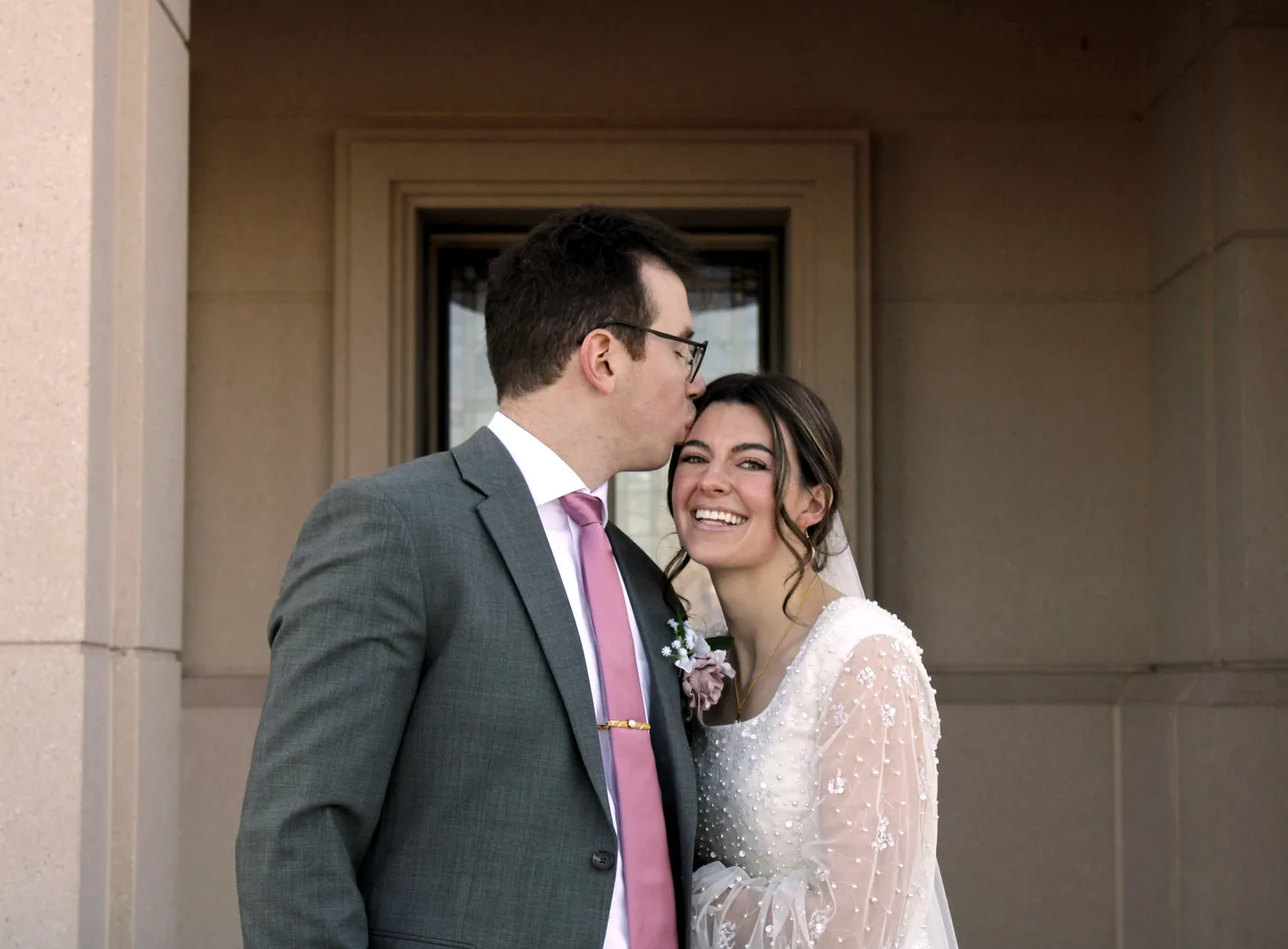 Groom kissing his smiling bride's cheek outside a temple
