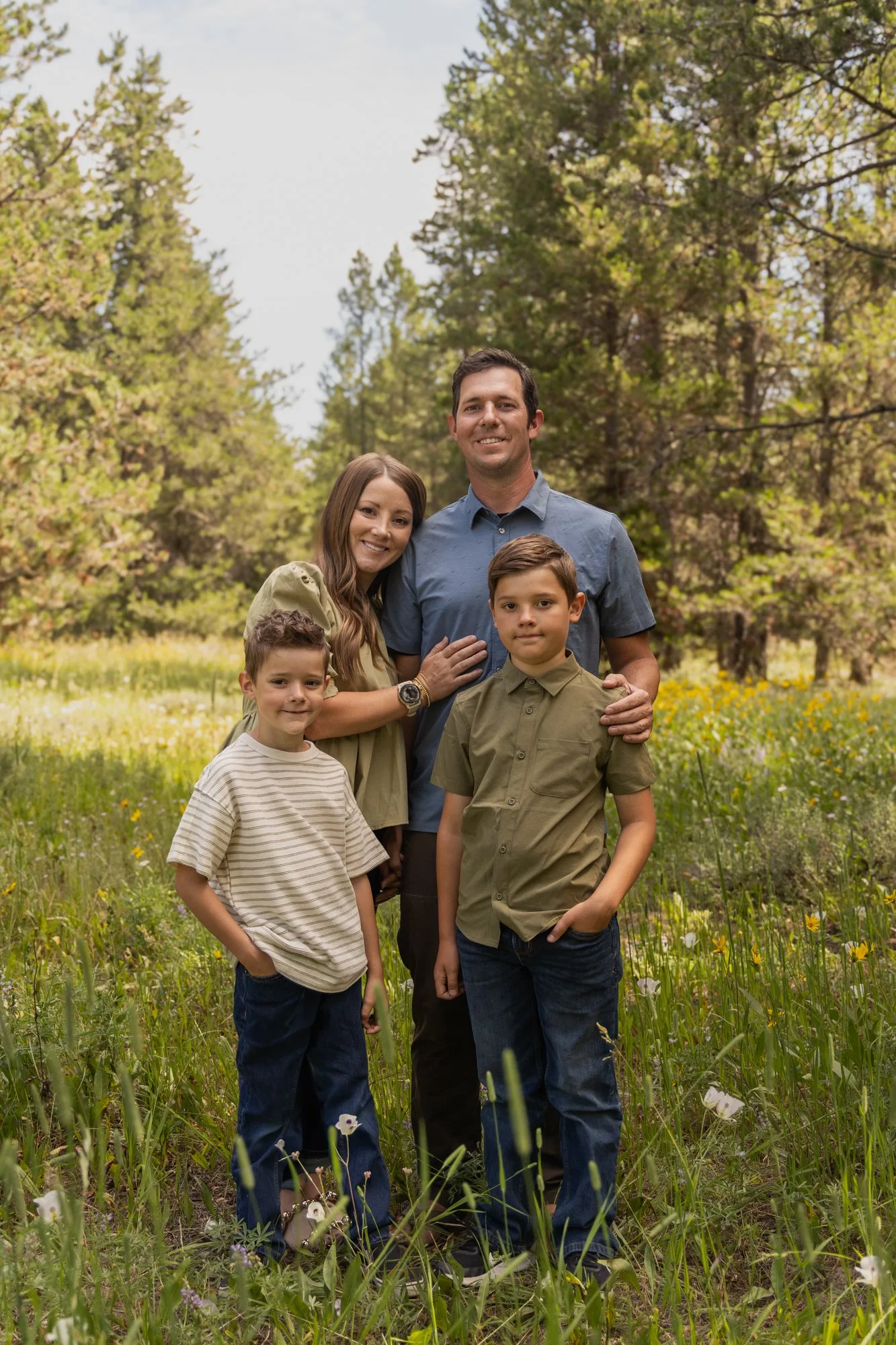 Parents and two sons standing in a sunny meadow among pine trees