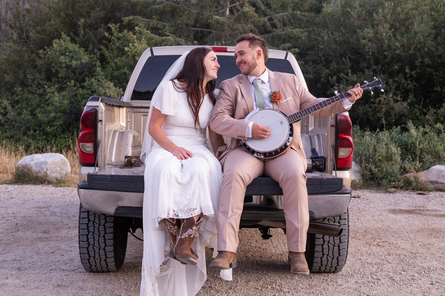 Bride and groom sitting on a pickup truck tailgate while the groom plays the banjo