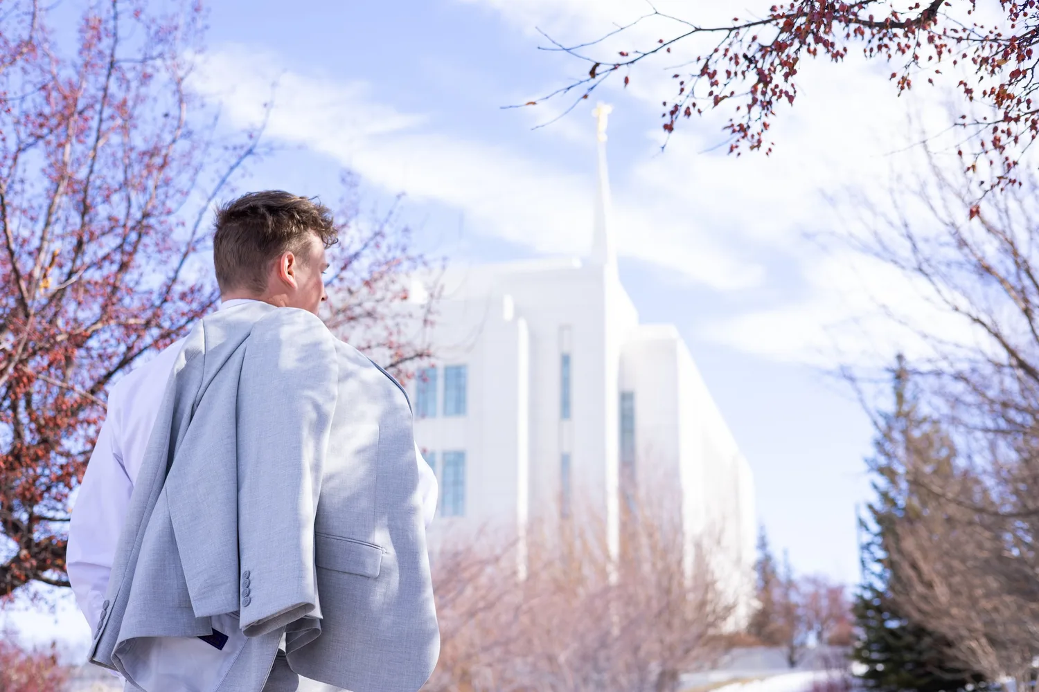 Missionary holding his suit jacket over his shoulder, looking toward a temple framed by blossoms