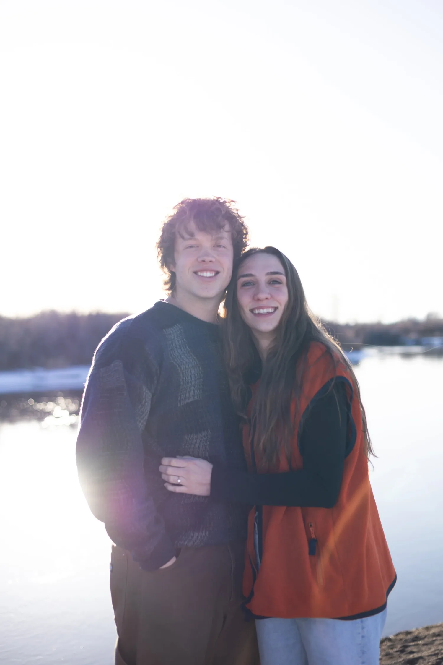 Couple hugging beside a sunlit lake in winter
