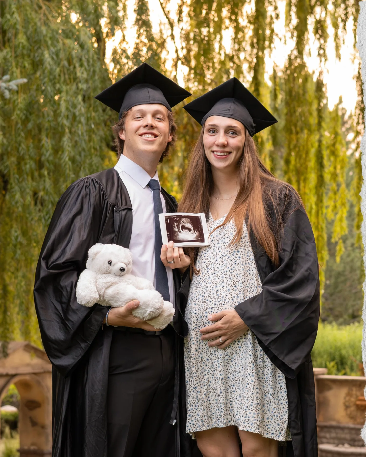 Graduating couple in black caps and gowns holding a teddy bear and an ultrasound photo