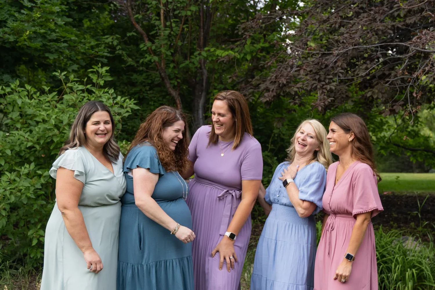 Five sisters laughing together in pastel dresses